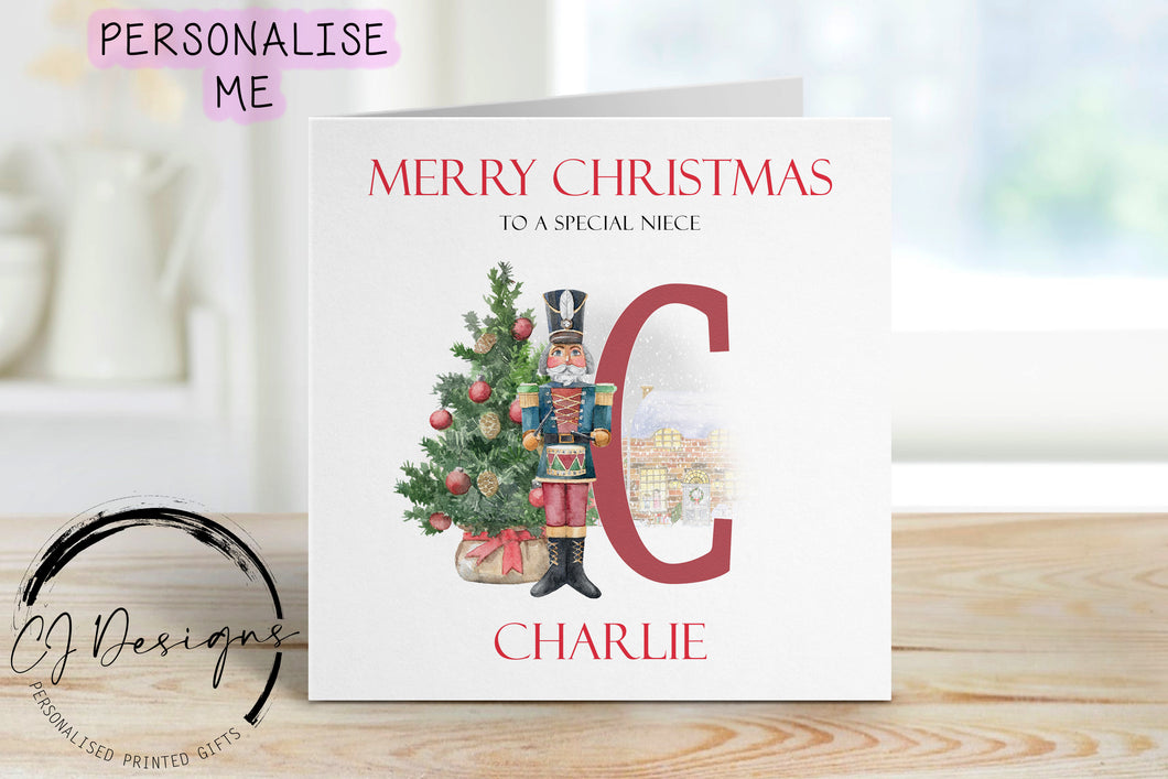 Niece personalised Christmas card with a nutcracker with Christmas Tree sstood next to a large red letter which depicts the first letter of your little